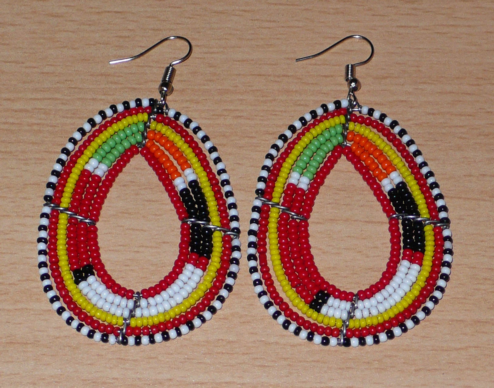 Boucles d'oreilles africaines aux motifs traditionnels Massai composées de perles de rocaille rouges et multicolores enfilées sur des fils de fer montés en forme de gouttes. Elles mesurent 7,5 cm de long et 4 cm de large et se portent avec des crochets en acier inoxydable.