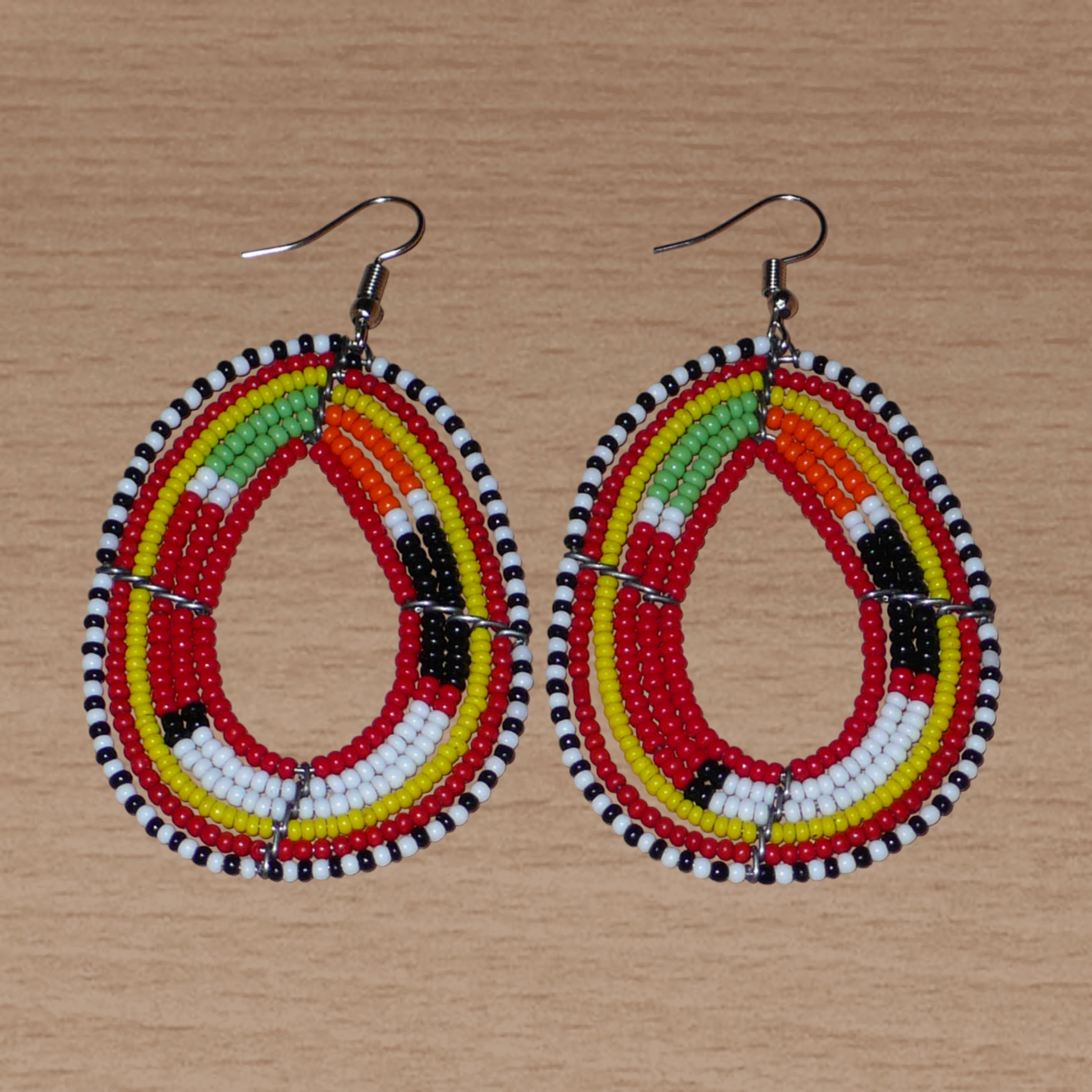 Boucles d'oreilles africaines aux motifs traditionnels Massai composées de perles de rocaille rouges et multicolores enfilées sur des fils de fer montés en forme de gouttes. Elles mesurent 7,5 cm de long et 4 cm de large et se portent avec des crochets en acier inoxydable.