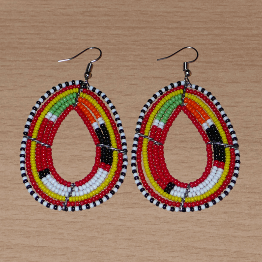 Boucles d'oreilles africaines aux motifs traditionnels Massai composées de perles de rocaille rouges et multicolores enfilées sur des fils de fer montés en forme de gouttes. Elles mesurent 7,5 cm de long et 4 cm de large et se portent avec des crochets en acier inoxydable.