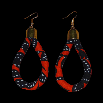 Longues boucles d'oreilles africaines tubulaires en forme de gouttes composées de bandes de tissu africain orange et noir avec des touches de blanc. Elles mesurent 9 cm de long et 4 cm de large et se portent avec des crochets en acier inoxydable sur des oreilles percées.
