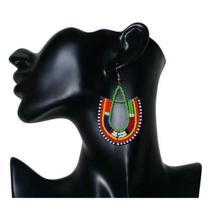 Boucles d'oreilles ethniques en forme d'ancres, confectionnées à la main par des artisans passionnés, composées de perles de rocaille vertes et multicolores glissées sur des structures géométriques en fils de fer. Elles mesurent 7.5 cm de long et 4.5 cm de large et se portent avec des crochets en acier inoxydable sur des oreilles percées. 