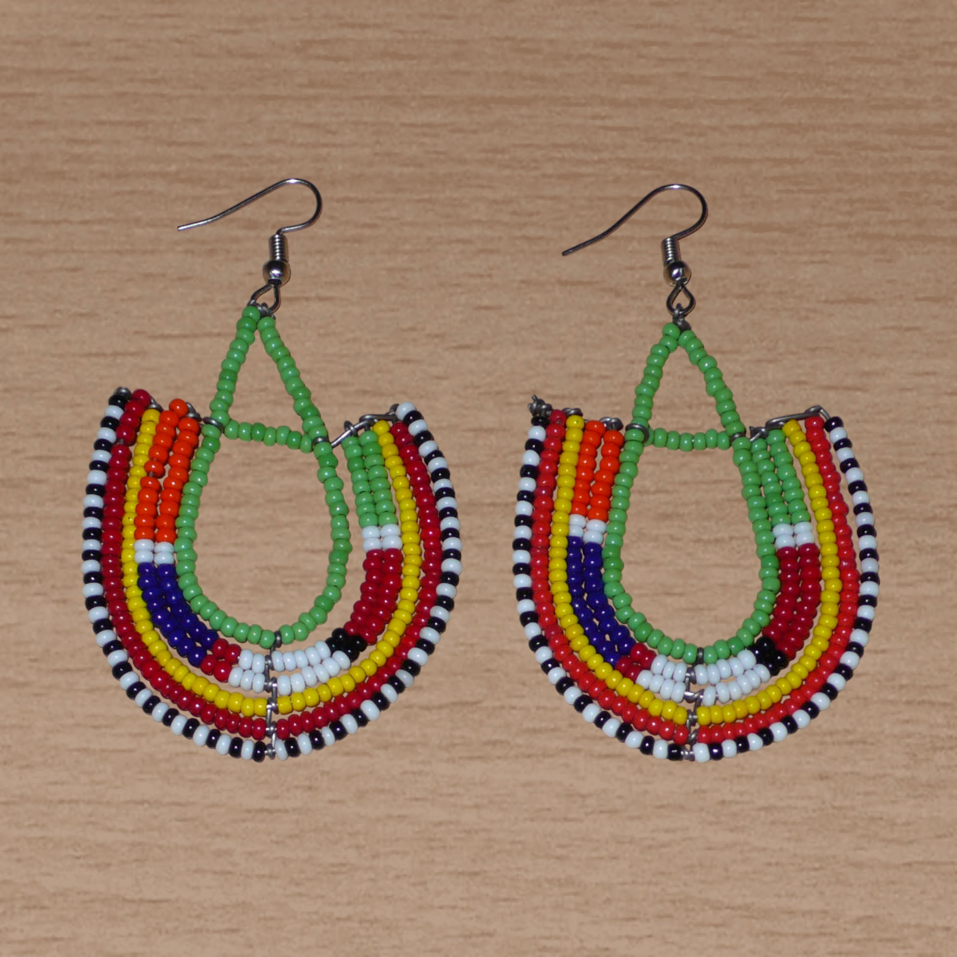 Boucles d'oreilles ethniques en forme d'ancres, confectionnées à la main par des artisans passionnés, composées de perles de rocaille vertes et multicolores glissées sur des structures géométriques en fils de fer. Elles mesurent 7.5 cm de long et 4.5 cm de large et se portent avec des crochets en acier inoxydable sur des oreilles percées. 