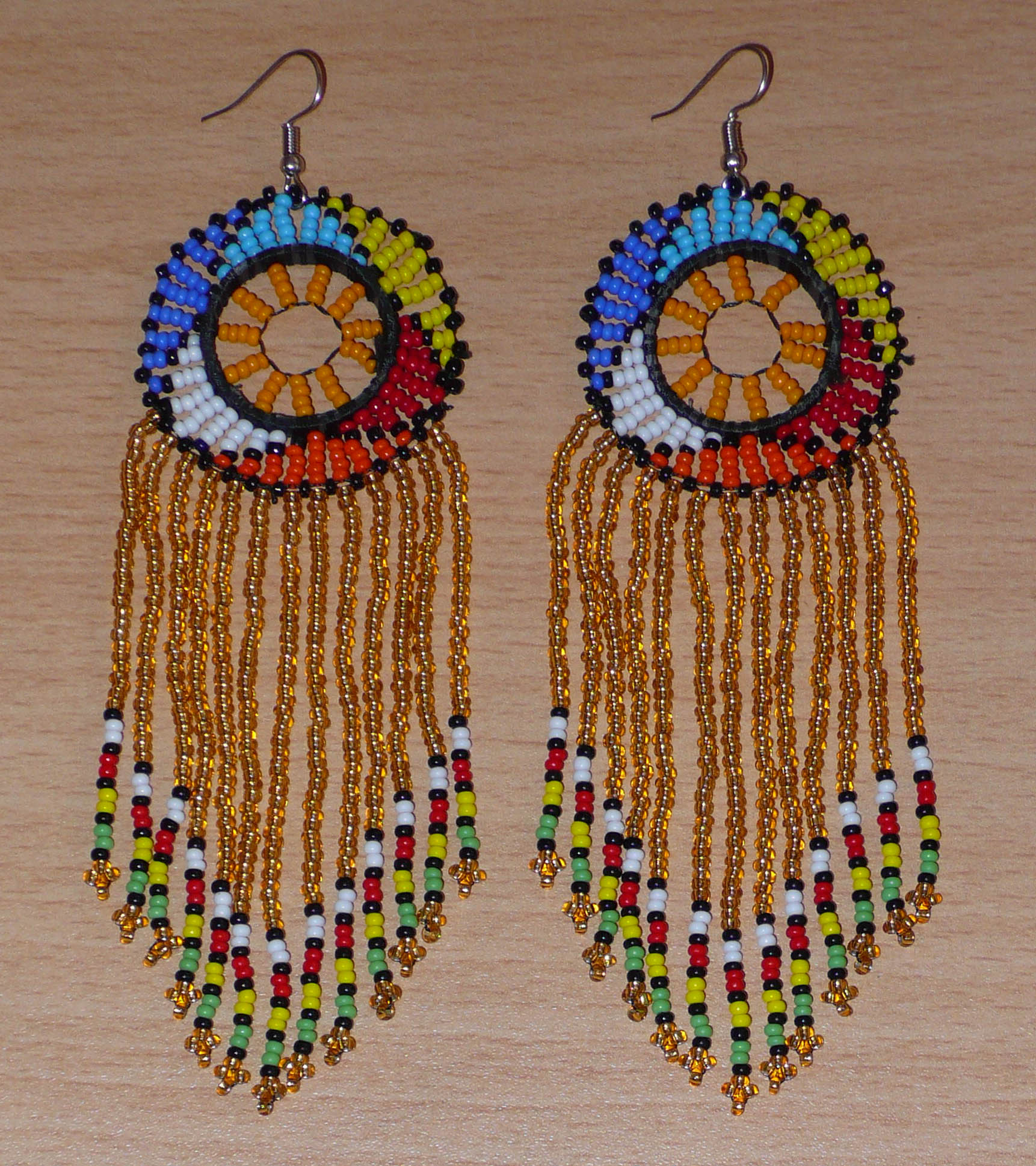 Boucles d'oreilles sud-africaines à franges et motifs traditionnels composées de perles de rocaille translucides dorées et multicolores. Elles mesurent 14,5 cm de long et 4,5 cm de large.