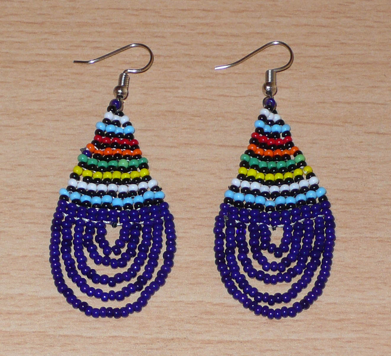 Boucles d'oreilles africaines traditionnelles zouloues en forme de gouttes composées de perles de rocaille bleu foncé et multicolores. Elles mesurent 7 cm de long et 2.5 cm de large, et se portent sur des oreilles percées.