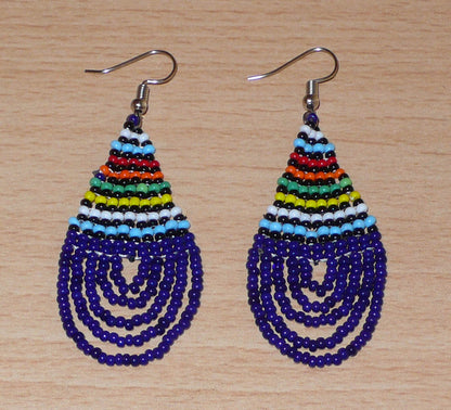 Boucles d'oreilles africaines traditionnelles zouloues en forme de gouttes composées de perles de rocaille bleu foncé et multicolores. Elles mesurent 7 cm de long et 2.5 cm de large, et se portent sur des oreilles percées.