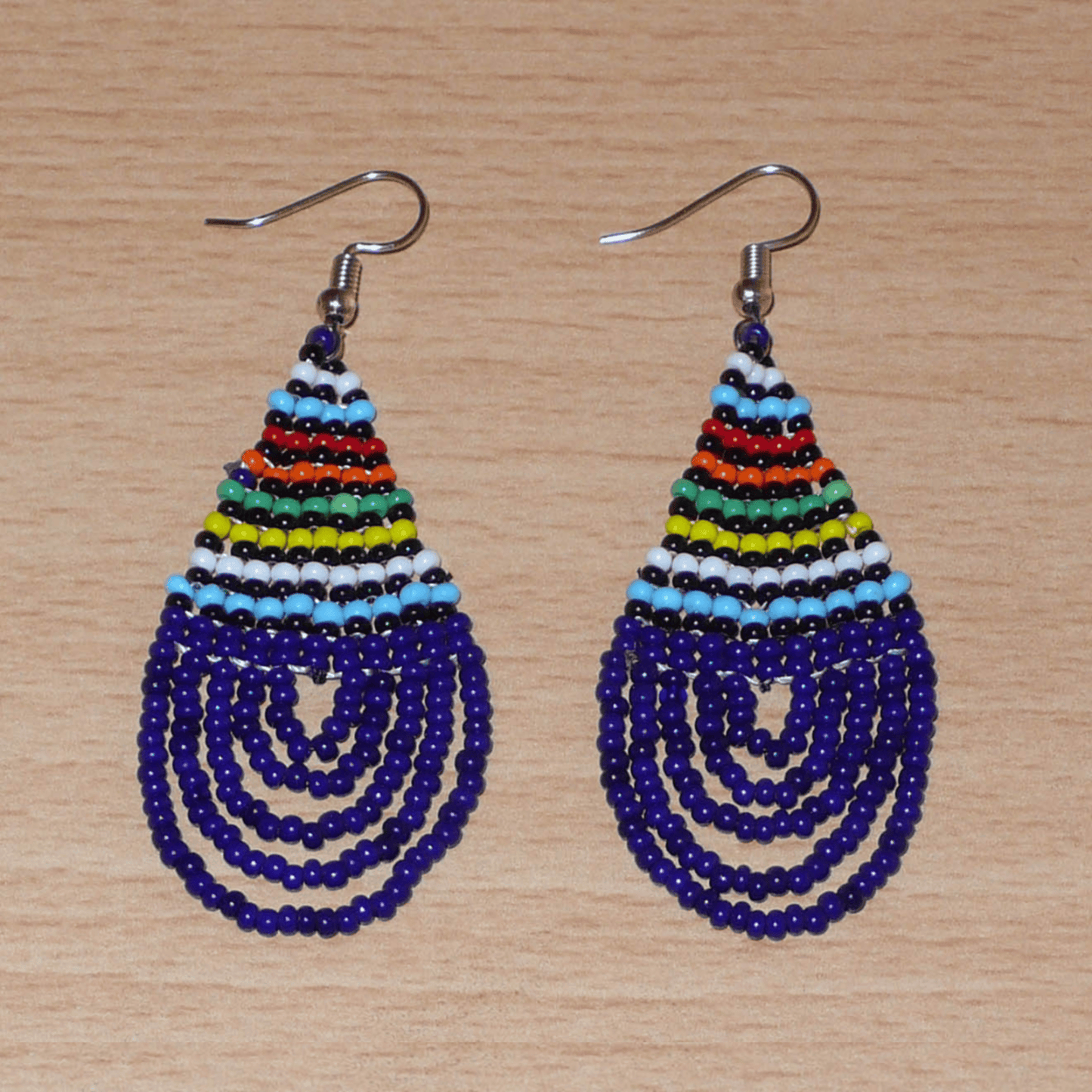 Boucles d'oreilles africaines zouloues en perles de rocaille bleu foncé et multicolores montées en forme de gouttes. Elles mesurent 7 cm de long et 2,5 cm de large, et se portent sur des oreilles percées.