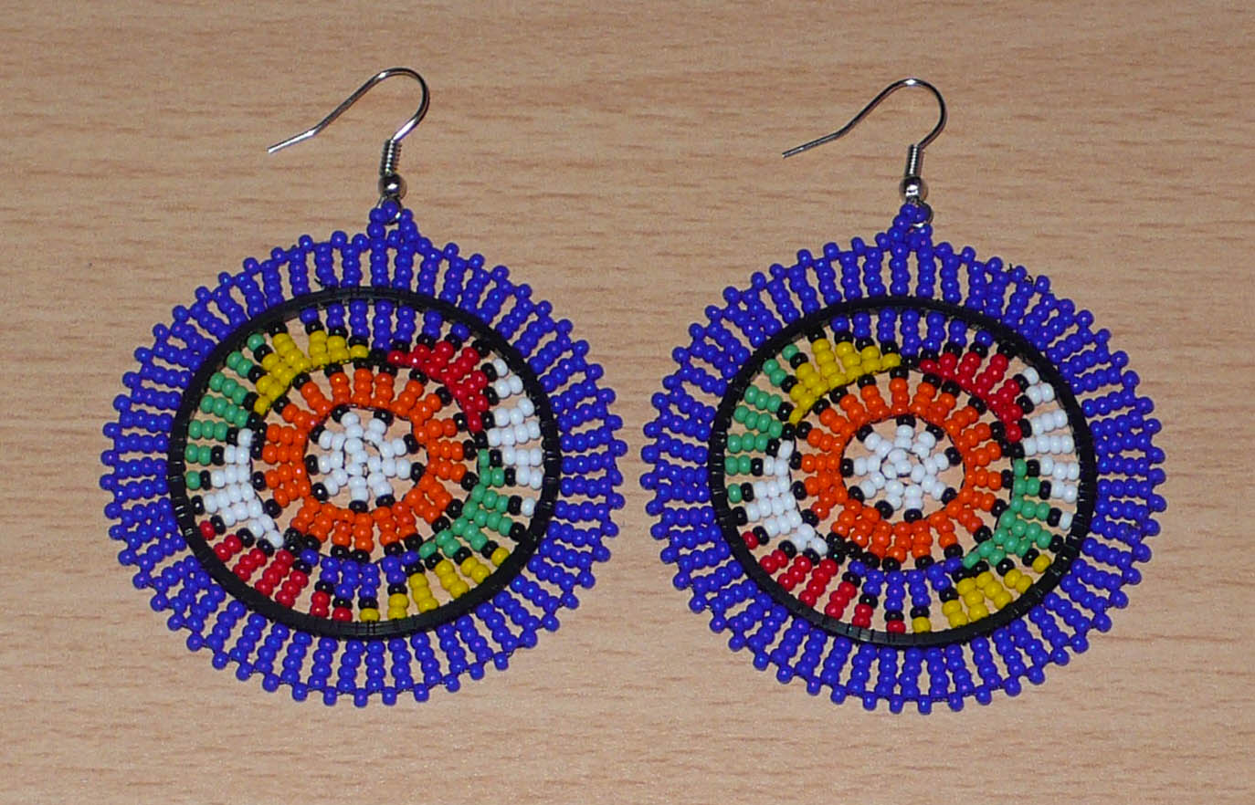 Boucles d'oreilles sud-africaines rondes à motifs ethniques zoulous composées de perles de rocaille bleues et multicolores. Elles mesurent 7,5 cm de long et 5,5 cm de large et se portent avec des crochets en acier inoxydable sur des oreilles percées.