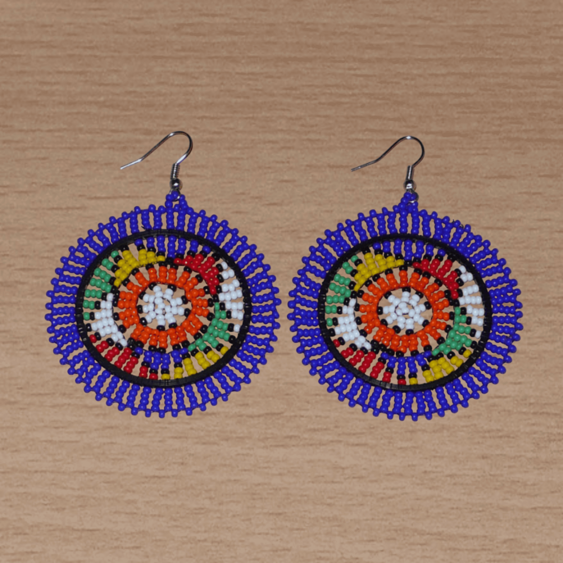 Boucles d'oreilles sud-africaines rondes à motifs ethniques zoulous composées de perles de rocaille bleues et multicolores. Elles mesurent 7,5 cm de long et 5,5 cm de large et se portent avec des crochets en acier inoxydable sur des oreilles percées.