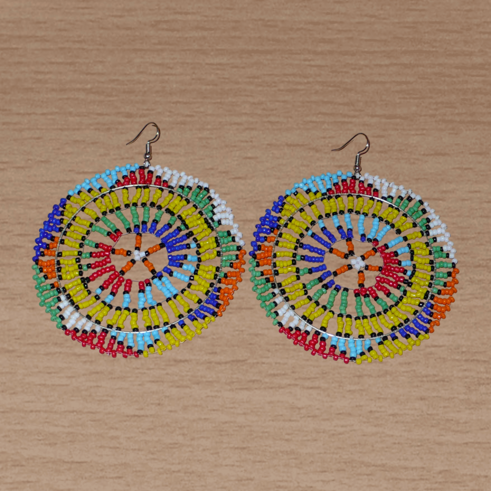 Boucles d'oreilles sud-africaines rondes au style afro chic des années 70. Elles se composent de perles de rocaille multicolores enfilées sur des fils de nylon fixés sur des structures circulaires. Surdimensionnées, elles mesurent 10 cm de long et 8,5 cm de large, et se portent sur des oreilles percées.