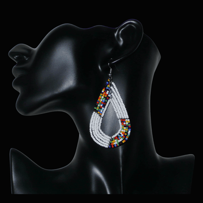 Boucles d'oreilles africaines multi-rangs blanches et multicolores aux accents évoquant le style bohème des années 70. Fabriquées au Kenya, elles se composent de perles de rocaille blanches et d'un mélange de perles multicolores glissées sur cinq rangées de fils de fer en forme de gouttes légèrement triangulaires. Ces boucles d'oreilles mesurent 8 cm de long et 4 cm de large ; elles se portent avec des crochets en acier inoxydable sur des oreilles percées.