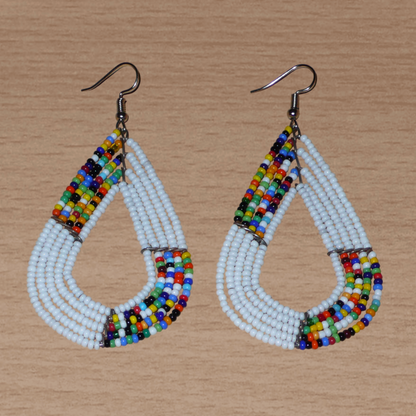 Boucles d'oreilles africaines multi-rangs blanches et multicolores aux accents évoquant le style bohème des années 70. Fabriquées au Kenya, elles se composent de perles de rocaille blanches et d'un mélange de perles multicolores glissées sur cinq rangées de fils de fer en forme de gouttes légèrement triangulaires. Ces boucles d'oreilles mesurent 8 cm de long et 4 cm de large ; elles se portent avec des crochets en acier inoxydable sur des oreilles percées.