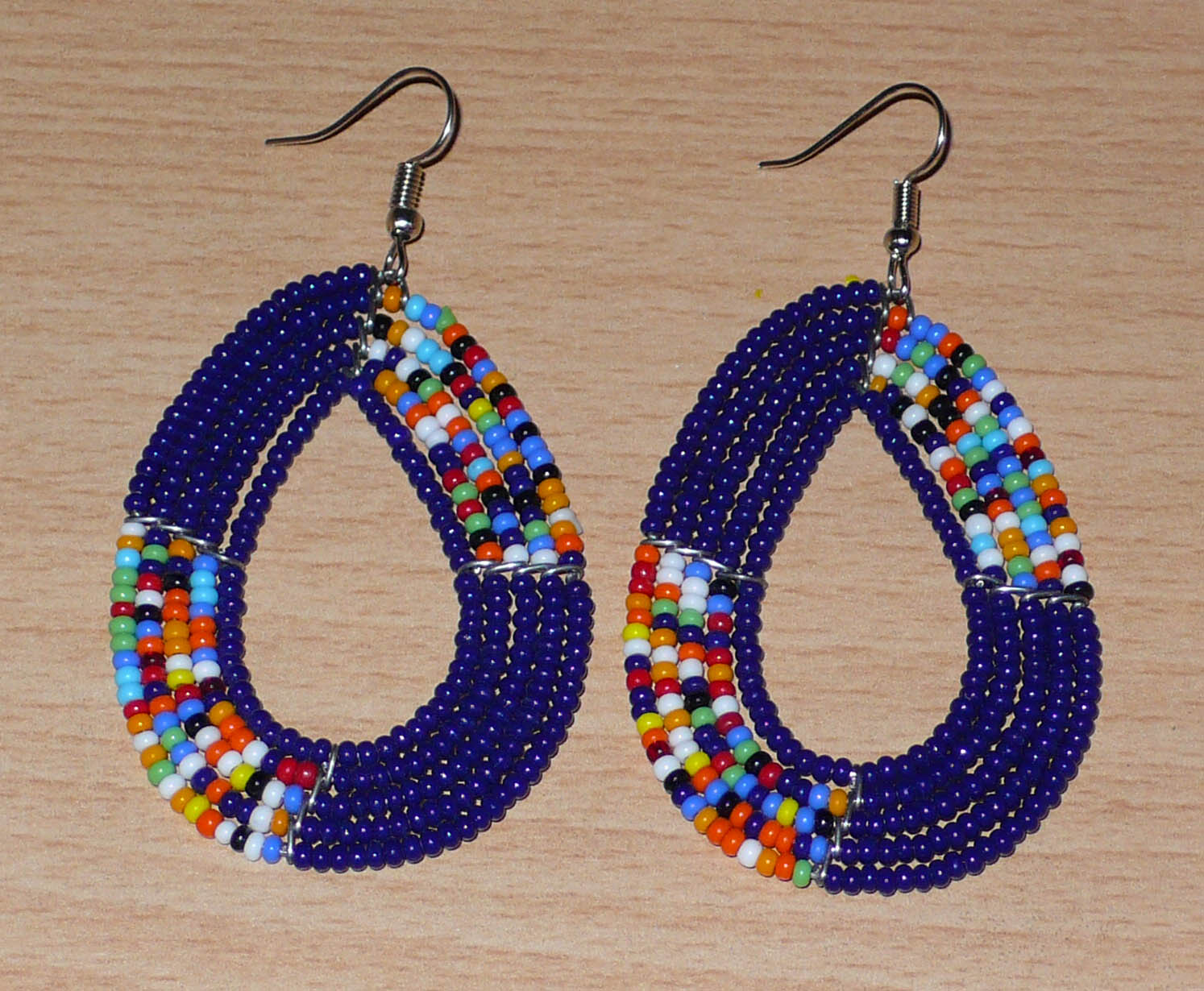 Boucles d'oreilles afro bohème bleu marine et multicolores en forme de gouttes composées de perles de rocaille. Elles mesurent 7,5 cm de long et 4 cm de large, et se portent sur des oreilles percées.