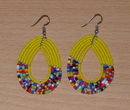 Boucles d'oreilles multi-rangs jaunes et multicolores faites de perles de rocaille enfilées sur cinq rangées de fils de fer montés en forme de gouttes. Elles mesurent 7 cm de long et 3,5 cm de large et se portent sur des oreilles percées.