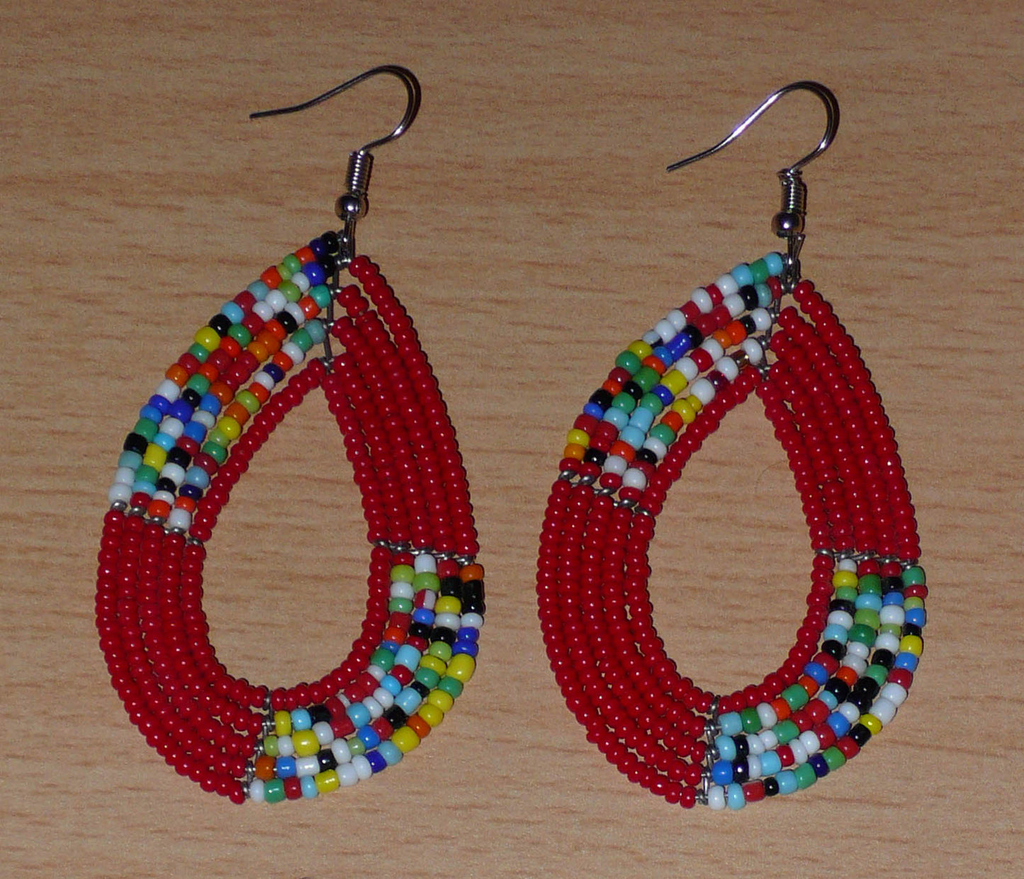 Boucles d'oreilles kenyanes multi-rangs rouges et multicolores composées de perles de rocaille montées en forme de gouttes. Elles mesurent 8 cm de long et 4 cm de large et se portent sur des oreilles percées.