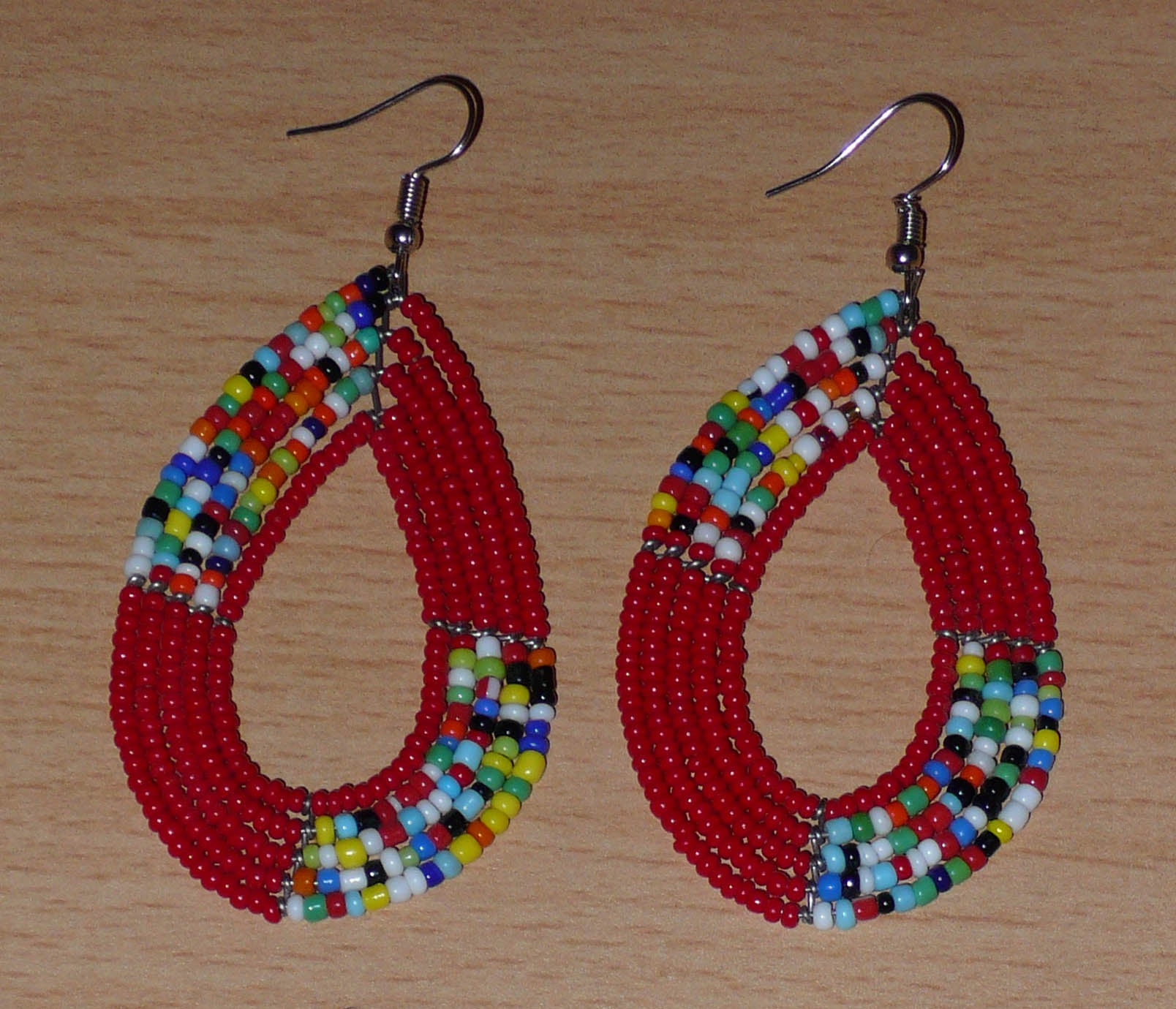 Boucles d'oreilles kenyanes multi-rangs rouges et multicolores composées de perles de rocaille montées en forme de gouttes. Elles mesurent 8 cm de long et 4 cm de large et se portent sur des oreilles percées.
