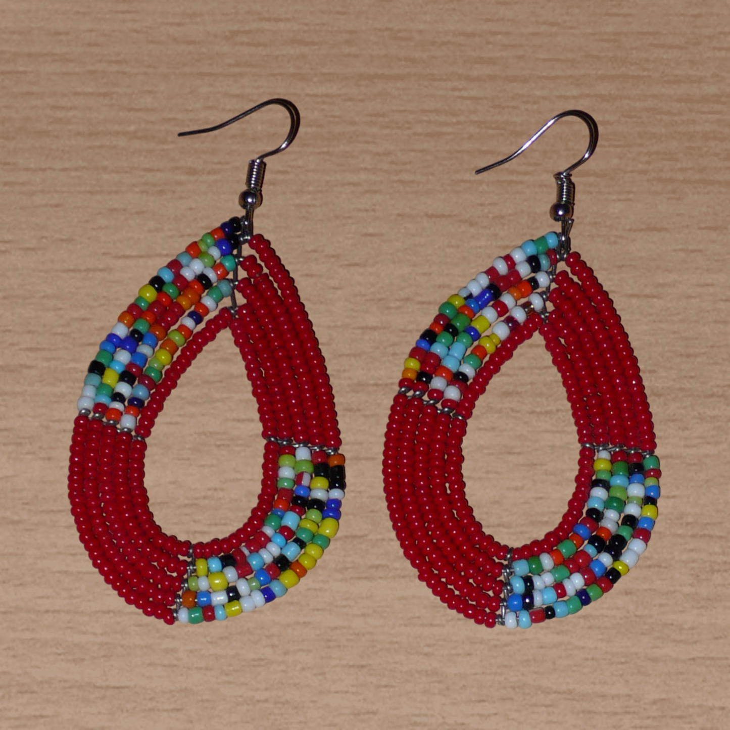 Boucles d'oreilles kenyanes multi-rangs rouges et multicolores composées de perles de rocaille montées en forme de gouttes. Elles mesurent 8 cm de long et 4 cm de large et se portent sur des oreilles percées.