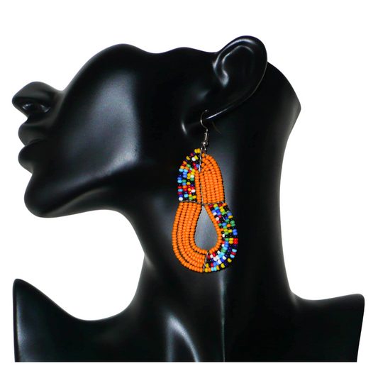 Boucles d'oreilles africaines de tradition artisanale kenyane, composées de perles de rocaille orange et multicolores fixées sur plusieurs rangées de fils de fer montés en forme de poires. Ces boucles d'oreilles, aux accents afro bohème, mesurent 8 cm de long et 3.5 cm de large ; elles se portent avec des crochets en acier inoxydable sur des oreilles percées. 