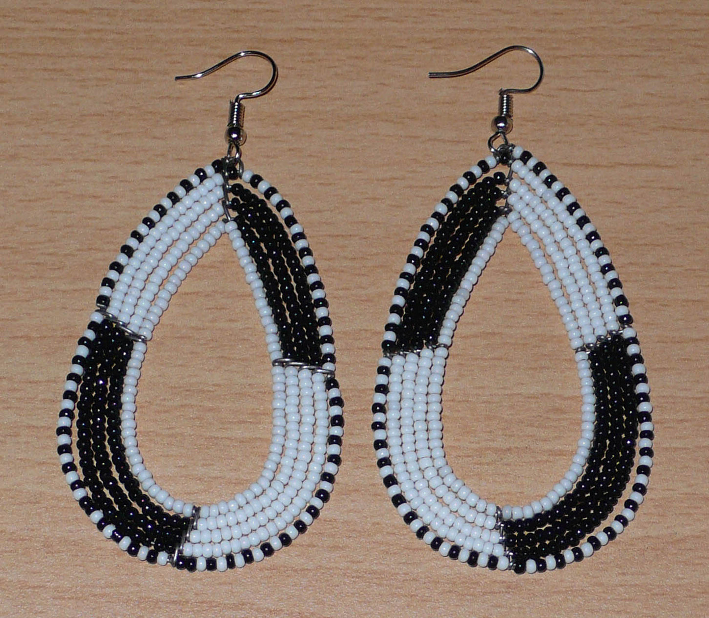 Longues boucles d'oreilles kenyanes en perles de rocaille blanches et noires enfilées sur plusieurs rangées de fils de fer montés en forme de gouttes. Ces boucles d'oreilles bicolores mesurent 8 cm de long et 4 cm de large et se portent avec des crochets en acier inoxydable sur des oreilles percées.