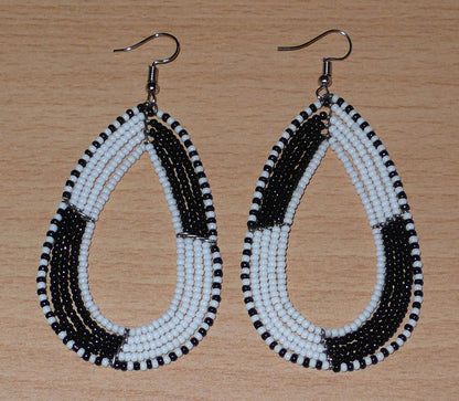 Longues boucles d'oreilles kenyanes en perles de rocaille blanches et noires enfilées sur plusieurs rangées de fils de fer montés en forme de gouttes. Ces boucles d'oreilles bicolores mesurent 8 cm de long et 4 cm de large et se portent avec des crochets en acier inoxydable sur des oreilles percées.