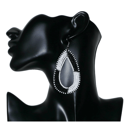 Longues boucles d'oreilles kenyanes en perles de rocaille blanches et noires enfilées sur plusieurs rangées de fils de fer montés en forme de gouttes. Ces boucles d'oreilles bicolores mesurent 8 cm de long et 4 cm de large et se portent avec des crochets en acier inoxydable sur des oreilles percées.