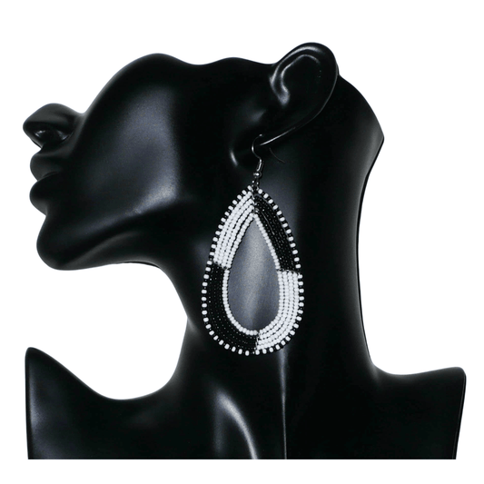 Longues boucles d'oreilles kenyanes en perles de rocaille blanches et noires enfilées sur plusieurs rangées de fils de fer montés en forme de gouttes. Ces boucles d'oreilles bicolores mesurent 8 cm de long et 4 cm de large et se portent avec des crochets en acier inoxydable sur des oreilles percées.