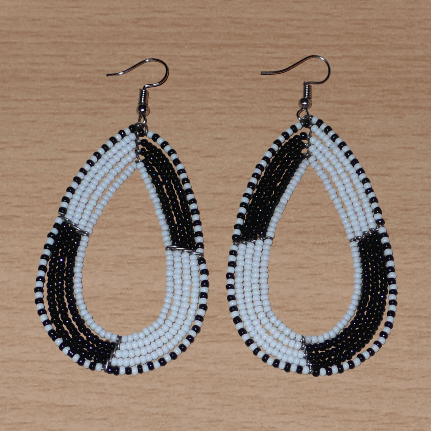 Longues boucles d'oreilles kenyanes en perles de rocaille blanches et noires enfilées sur plusieurs rangées de fils de fer montés en forme de gouttes. Ces boucles d'oreilles bicolores mesurent 8 cm de long et 4 cm de large et se portent avec des crochets en acier inoxydable sur des oreilles percées.