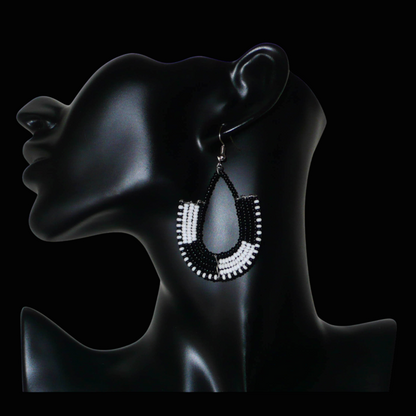 Boucles d'oreilles bicolores kenyanes en forme d'ancres, composées de perles de rocaille noires et blanches. Elles mesurent 7 cm de long et 4 cm de large, et se portent sur des oreilles percées.