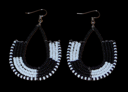 Boucles d'oreilles bicolores kenyanes en forme d'ancres, composées de perles de rocaille noires et blanches. Elles mesurent 7 cm de long et 4 cm de large, et se portent sur des oreilles percées.