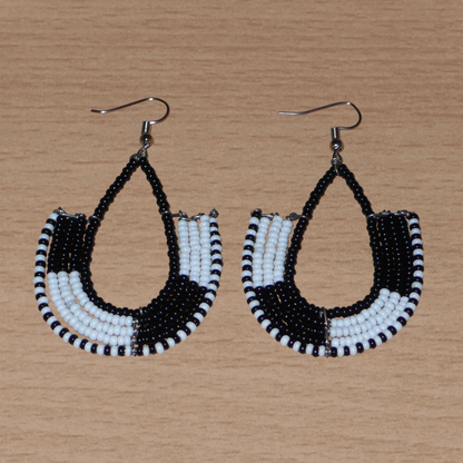 Boucles d'oreilles bicolores kenyanes en forme d'ancres, composées de perles de rocaille noires et blanches. Elles mesurent 7 cm de long et 4 cm de large, et se portent sur des oreilles percées.