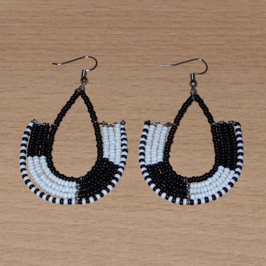 Boucles d'oreilles bicolores kenyanes en forme d'ancres, composées de perles de rocaille noires et blanches. Elles mesurent 7 cm de long et 4 cm de large, et se portent sur des oreilles percées.