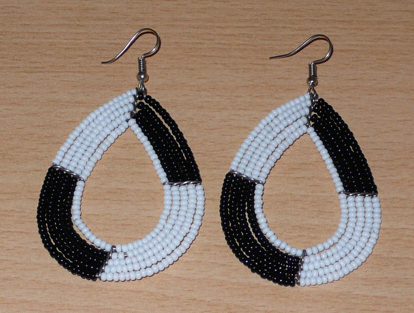 Longues boucles d'oreilles bicolores noires et blanches en forme de gouttes faites de perles de rocaille ; elles mesurent 8 cm de long et 4 cm de large, et se portent sur des oreilles percées.
