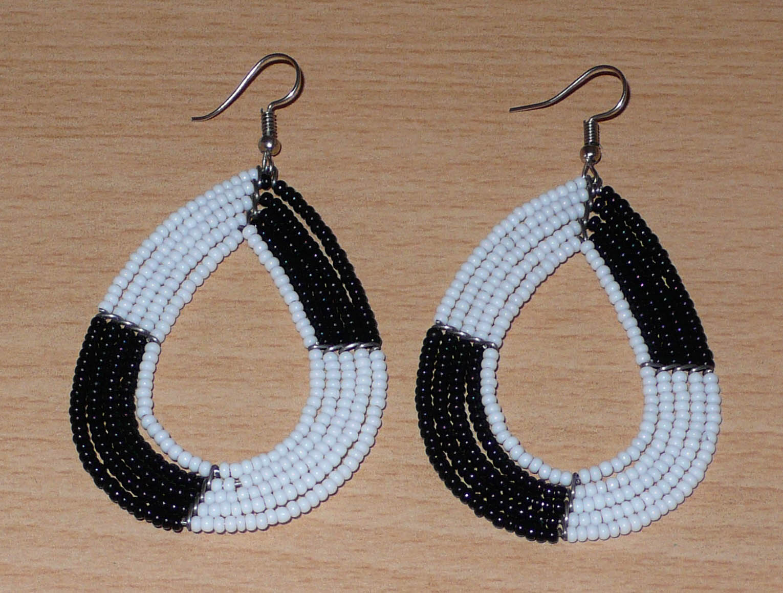 Longues boucles d'oreilles bicolores noires et blanches en forme de gouttes faites de perles de rocaille ; elles mesurent 8 cm de long et 4 cm de large, et se portent sur des oreilles percées.