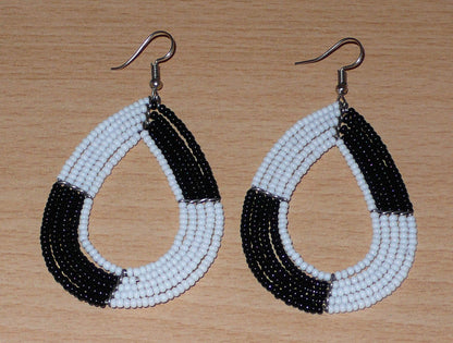 Longues boucles d'oreilles bicolores noires et blanches en forme de gouttes faites de perles de rocaille ; elles mesurent 8 cm de long et 4 cm de large, et se portent sur des oreilles percées.