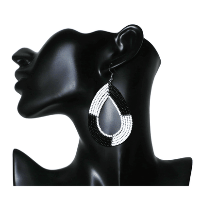 Longues boucles d'oreilles bicolores noires et blanches en forme de gouttes faites de perles de rocaille ; elles mesurent 8 cm de long et 4 cm de large, et se portent sur des oreilles percées.