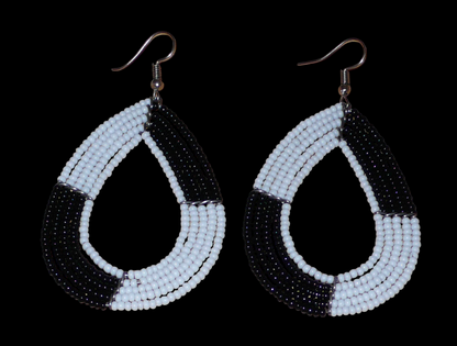 Longues boucles d'oreilles bicolores noires et blanches en forme de gouttes faites de perles de rocaille ; elles mesurent 8 cm de long et 4 cm de large, et se portent sur des oreilles percées.