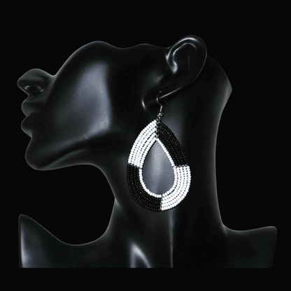 Longues boucles d'oreilles bicolores noires et blanches en forme de gouttes faites de perles de rocaille ; elles mesurent 8 cm de long et 4 cm de large, et se portent sur des oreilles percées.