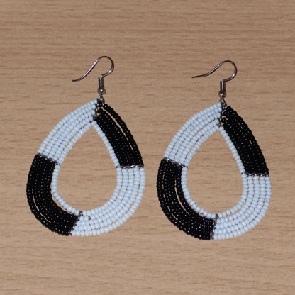 Longues boucles d'oreilles bicolores noires et blanches en forme de gouttes faites de perles de rocaille ; elles mesurent 8 cm de long et 4 cm de large, et se portent sur des oreilles percées.