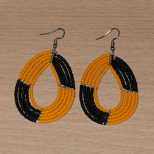 Boucles d'oreilles kenyanes bicolores multi-rangs en perles de rocaille orange et noires montées en forme de gouttes. Elles mesurent 7.5 cm de long et 4 cm de large et se portent sur des oreilles percées.