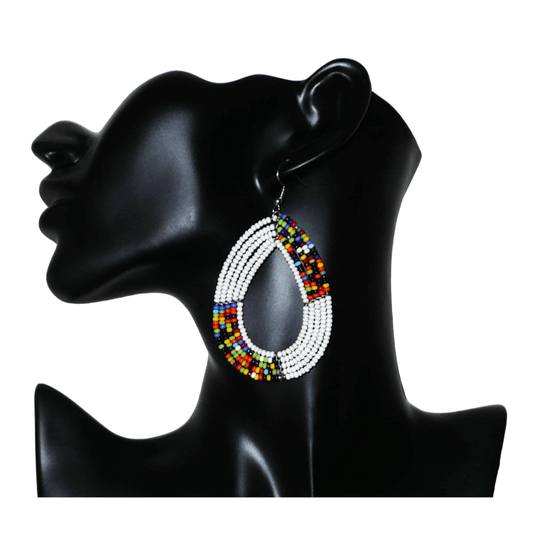 Boucles d'oreilles ethniques fabriquées au Kenya faites de perles de rocaille blanches et multicolores enfilées sur cinq rangées de fils de fer montés en forme de gouttes. Elles mesurent 8 cm de long et 4,5 cm de large et se portent sur des oreilles percées.