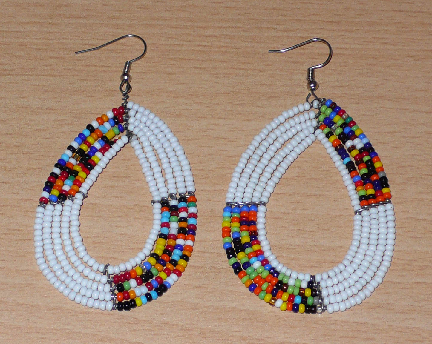 Boucles d'oreilles ethniques fabriquées au Kenya faites de perles de rocaille blanches et multicolores enfilées sur cinq rangées de fils de fer montés en forme de gouttes. Elles mesurent 8 cm de long et 4,5 cm de large et se portent sur des oreilles percées.