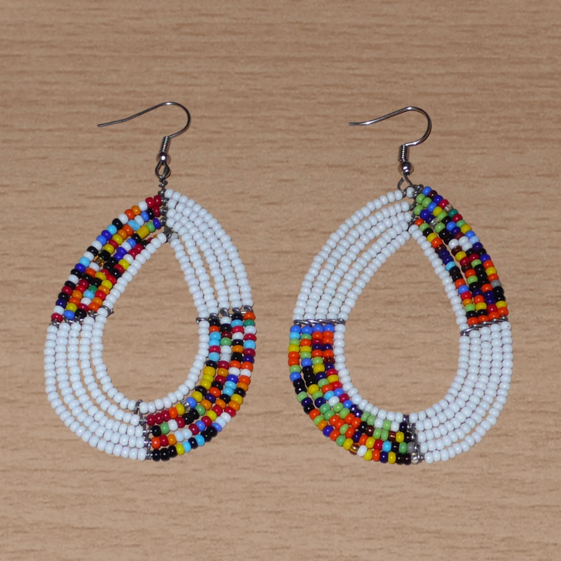 Boucles d'oreilles ethniques fabriquées au Kenya faites de perles de rocaille blanches et multicolores enfilées sur cinq rangées de fils de fer montés en forme de gouttes. Elles mesurent 8 cm de long et 4,5 cm de large et se portent sur des oreilles percées.