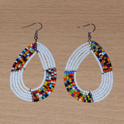 Boucles d'oreilles ethniques fabriquées au Kenya faites de perles de rocaille blanches et multicolores enfilées sur cinq rangées de fils de fer montés en forme de gouttes. Elles mesurent 8 cm de long et 4,5 cm de large et se portent sur des oreilles percées.