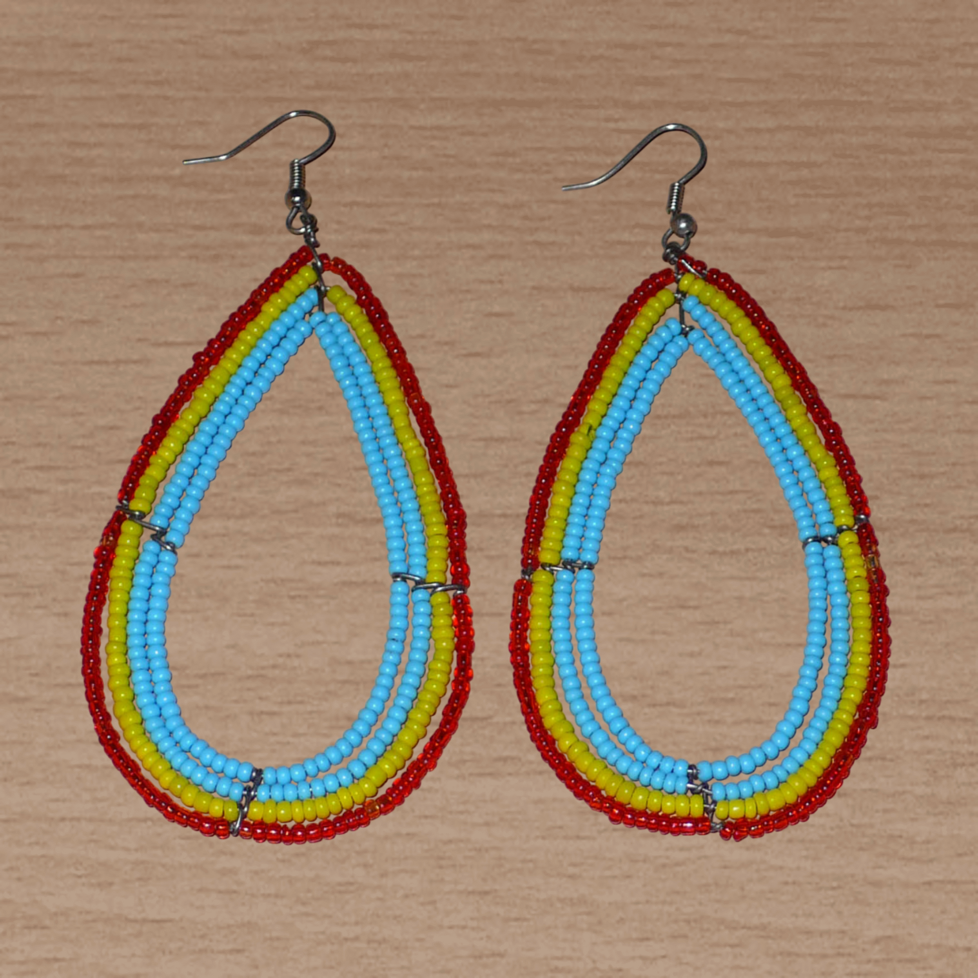 Longues et larges boucles d'oreilles aux couleurs exotiques composées de perles bleu turquoise, jaunes et rouges translucides enfilées sur quatre rangées de fils de fer montés en forme de gouttes. Ces boucles d'oreilles surdimensionnées mesurent 9,5 cm de long et 4,5 cm de large ; elles se portent avec des crochets sur des oreilles percées.