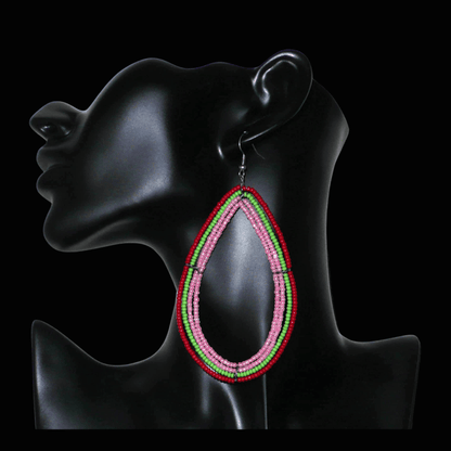 Boucles d'oreilles "oversized" composées de perles de rocaille rose nacré, vertes et rouges enfilées sur quatre rangées de fils de fer montés en forme de gouttes. Surdimensionnées, ces boucles d'oreilles mesurent 11 cm de long et 5,5 cm de large ; elles se portent avec des crochets en acier inoxydable sur des oreilles percées.
