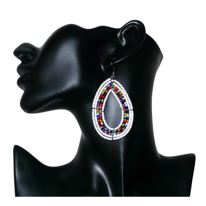 Boucles d'oreilles bohème blanches et multicolores en forme de gouttes faites de perles de rocaille. Elles mesurent 7,5 cm de long et 4 cm de large et se portent sur des oreilles percées.