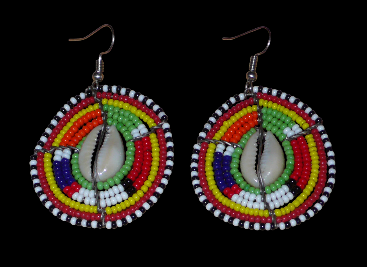 Boucles d'oreilles africaines ethniques aux motifs tribaux traditionnels caractéristiques de l'artisanat Massai. Confectionnées au Kenya, elles sont composées de perles de rocaille vertes et multicolores et de coquillages cauris fixés sur des fils de fer montés en forme de boucliers Massai. De taille moyenne, elles mesurent 6 cm de long et 4 cm de large, et se portent avec des crochets en acier inoxydable sur des oreilles percées.