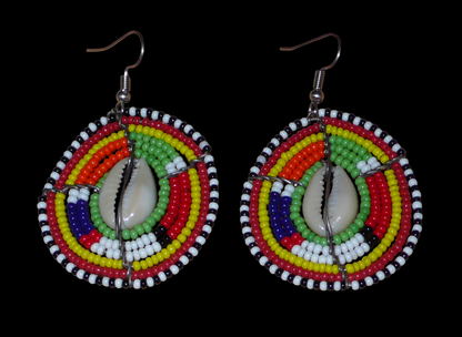 Boucles d'oreilles africaines ethniques aux motifs tribaux traditionnels caractéristiques de l'artisanat Massai. Confectionnées au Kenya, elles sont composées de perles de rocaille vertes et multicolores et de coquillages cauris fixés sur des fils de fer montés en forme de boucliers Massai. De taille moyenne, elles mesurent 6 cm de long et 4 cm de large, et se portent avec des crochets en acier inoxydable sur des oreilles percées.