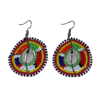 Boucles d'oreilles africaines ethniques aux motifs tribaux traditionnels caractéristiques de l'artisanat Massai. Confectionnées au Kenya, elles sont composées de perles de rocaille vertes et multicolores et de coquillages cauris fixés sur des fils de fer montés en forme de boucliers Massai. De taille moyenne, elles mesurent 6 cm de long et 4 cm de large, et se portent avec des crochets en acier inoxydable sur des oreilles percées.