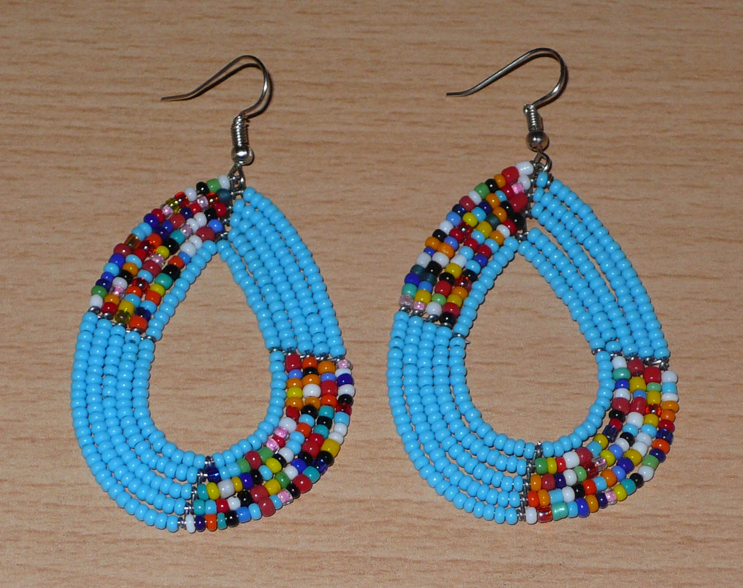 Boucles d'oreilles kenyanes multi-rangs en perles de rocaille bleu ciel et multicolores. Elles mesurent 7 cm de long et 4 cm de large et se portent sur des oreilles percées.