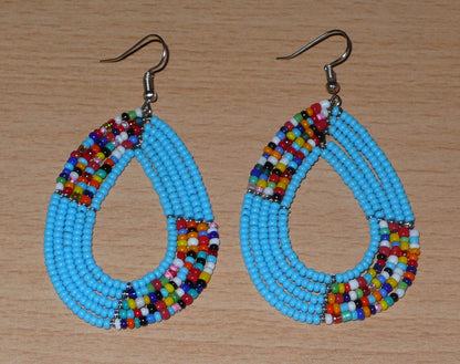 Boucles d'oreilles kenyanes multi-rangs en perles de rocaille bleu ciel et multicolores. Elles mesurent 7 cm de long et 4 cm de large et se portent sur des oreilles percées.